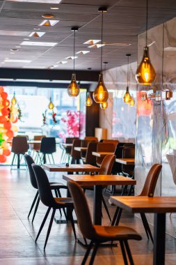 Konforlu ve modern kafe içi ahşap mobilyalar, sıcak ışıklandırma ve sokağa bakan büyük pencerelerle, davetkar bir atmosfer yaratıyor.