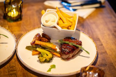 Kızarmış tavuk göğsü, patates kızartması ve soğan halkaları, ahşap çatal bıçaklı karton tepside. Çevre dostu tek kullanımlık plastik konteynır