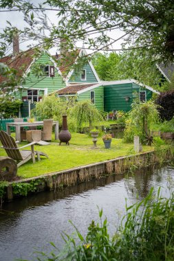 Hollanda tipik manzarası. Hollanda 'nın Zaanse Schans köyünde mavi bulutlu gökyüzüne karşı eski evleri olan geleneksel bir yel değirmeni. Ünlü turizm mekanı. Yeşil çimlerde otlayan koyunlar.