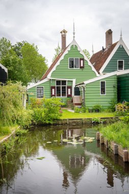 Hollanda tipik manzarası. Hollanda 'nın Zaanse Schans köyünde mavi bulutlu gökyüzüne karşı eski evleri olan geleneksel bir yel değirmeni. Ünlü turizm mekanı. Yeşil çimlerde otlayan koyunlar.