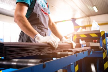 Bir fabrika işçisi çatı için metal profil çıkarıyor. Fabrikadaki işçiler metal profilli levhaları ölçüyor. Metal endüstrisi. Metal çatı üretimi, çatı elementlerinin üretimi