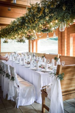 Büyük, uzun, süslü, ahşap bir masa örtüsü ve tabaklar, çiçekler, mumlar ile kaplı sandalyeler doğada ormanın yakınında duruyor. Düğün ziyafeti. ışık arkaplanı