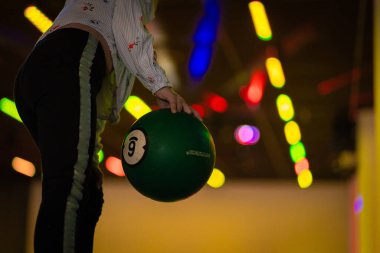 Renkli, iyi ışıklandırılmış bovling salonunda çeşitli topları ve bulanık arka planı olan hareketli bowling topuna uzanmak dinamik bir atmosfer yaratıyor.