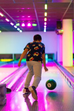 Mutlu genç çocuk bowling oynarken eğleniyor ve tezahürat yapıyor.