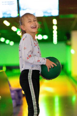 Küçük kız eğleniyor ve bowling oynuyor.
