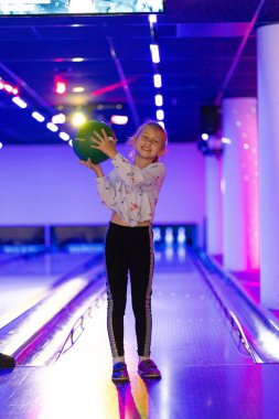 Küçük kız eğleniyor ve bowling oynuyor.