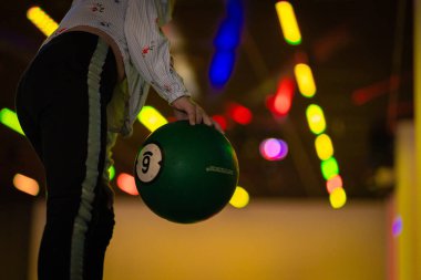 Renkli, iyi ışıklandırılmış bovling salonunda çeşitli topları ve bulanık arka planı olan hareketli bowling topuna uzanmak dinamik bir atmosfer yaratıyor.