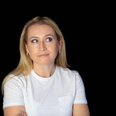 Çekici sarışın, parlak, beyaz tişörtlü, genç bir kadının fotoğrafı. Alnında boş boş boş duran, izole edilmiş siyah arka plan gülümsemesi.