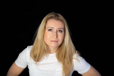 Çekici sarışın, parlak, beyaz tişörtlü, genç bir kadının fotoğrafı. Alnında boş boş boş duran, izole edilmiş siyah arka plan gülümsemesi.