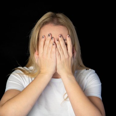 Gülümseyen sarışın modelin yüzünü elinin arkasına saklamasına sevindim. Geniş bir gülümsemesi var. Siyah arka planda izole edilmiş yakışıklı bir adamdan iltifat almaktan mutlu. Pozitif genç kadın