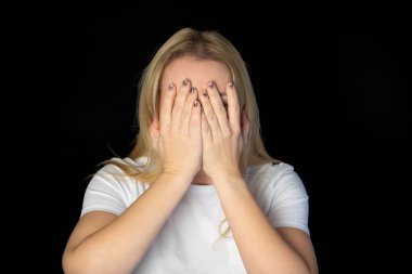 Gülümseyen sarışın modelin yüzünü elinin arkasına saklamasına sevindim. Geniş bir gülümsemesi var. Siyah arka planda izole edilmiş yakışıklı bir adamdan iltifat almaktan mutlu. Pozitif genç kadın