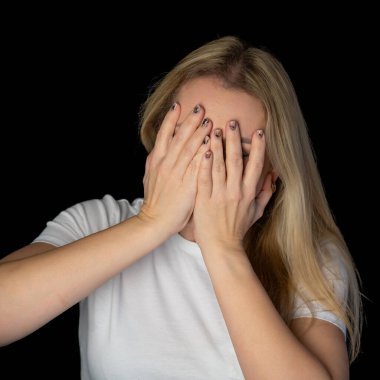 Gülümseyen sarışın modelin yüzünü elinin arkasına saklamasına sevindim. Geniş bir gülümsemesi var. Siyah arka planda izole edilmiş yakışıklı bir adamdan iltifat almaktan mutlu. Pozitif genç kadın