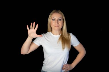 Siyah arka planda duran beyaz tişörtlü genç sarışın kadın parmaklarını göstererek rakamları gösteriyor. Beş numara. beş parmak