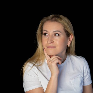 Çekici sarışın, parlak, beyaz tişörtlü, genç bir kadının fotoğrafı. Alnında boş boş boş duran, izole edilmiş siyah arka plan gülümsemesi.