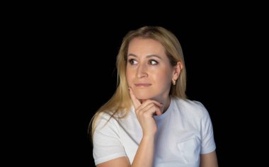 Çekici sarışın, parlak, beyaz tişörtlü, genç bir kadının fotoğrafı. Alnında boş boş boş duran, izole edilmiş siyah arka plan gülümsemesi.