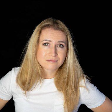 Çekici sarışın, parlak, beyaz tişörtlü, genç bir kadının fotoğrafı. Alnında boş boş boş duran, izole edilmiş siyah arka plan gülümsemesi.