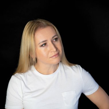 Çekici sarışın, parlak, beyaz tişörtlü, genç bir kadının fotoğrafı. Alnında boş boş boş duran, izole edilmiş siyah arka plan gülümsemesi.