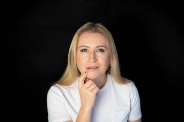 Çekici sarışın, parlak, beyaz tişörtlü, genç bir kadının fotoğrafı. Alnında boş boş boş duran, izole edilmiş siyah arka plan gülümsemesi.