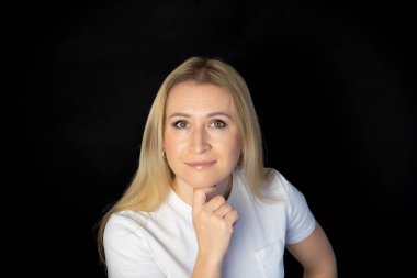 Çekici sarışın, parlak, beyaz tişörtlü, genç bir kadının fotoğrafı. Alnında boş boş boş duran, izole edilmiş siyah arka plan gülümsemesi.