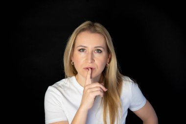 Gülümseyen ve çenesini kapatmak için işaret eden güzel sarışın bir kadının portresi. Kopyalama alanı ve kırpma yolu ile siyah arkaplanda izole edildi