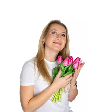 Beyaz tişörtlü güzel sarışın, olgun Avrupalı kadın elinde beyaz arka planda pembe mor laleler tutuyor.