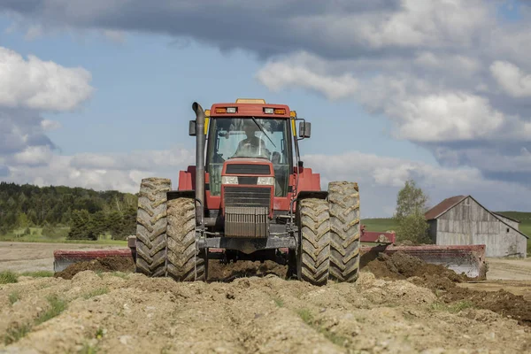 A farmer with the help of his powerful red tractor is pulling an agricultural land leveler in one of his fields on a beautiful spring day. Agriculture. Tractor. Farmland. Farming. Land leveler.