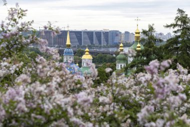 İlkbahar çiçekleri ve modern şehir siluetiyle çerçevelenmiş Ortodoks kilise kubbeleri
