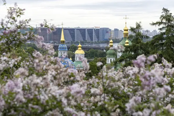 İlkbahar çiçekleri ve modern şehir siluetiyle çerçevelenmiş Ortodoks kilise kubbeleri