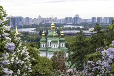 Kyiv manastırı kubbeleri bahar leylakları şehir silueti manzarasıyla çerçevelenmiştir.