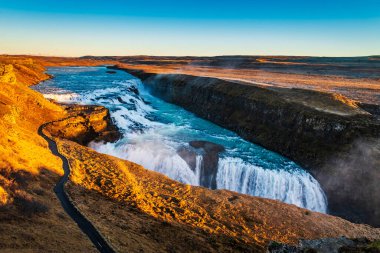 Gullfoss şelalesinin dramatik manzarası. Düşük güneş ışığı sisi aydınlatıyor.