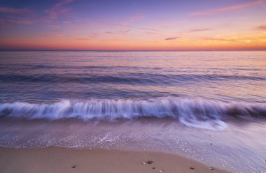 Bournemouth sahilindeki sakin sular gün batımında batan güneş tarafından aydınlatılıyor.
