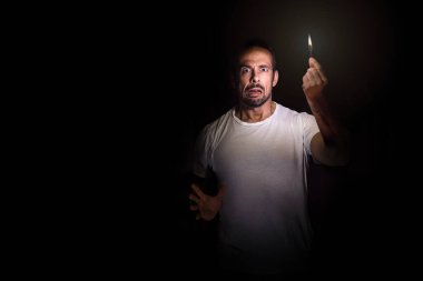 Karanlıkta elinde kibritle kameraya bakan endişeli bir adam. Karartma konsepti.