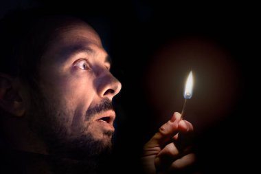 Worried man with a match in the dark. Blackout concept.