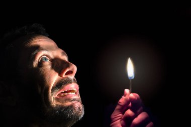 Worried man with a match in the dark. Blackout concept.