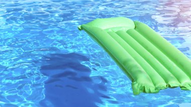 Mavi yüzme havuzunda yüzen yeşil şişme yatak..