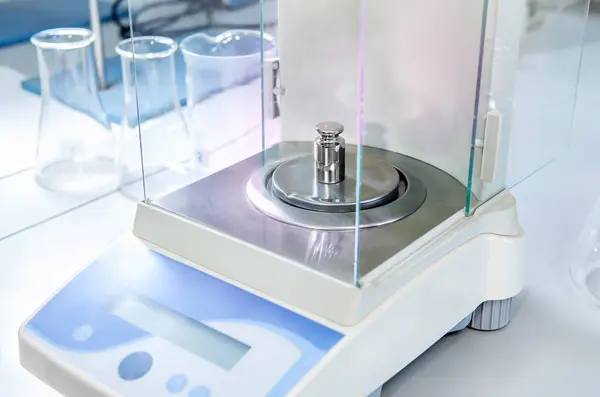 Analytical balance in a laboratory with a metal weight. Concept of laboratory balance calibration.