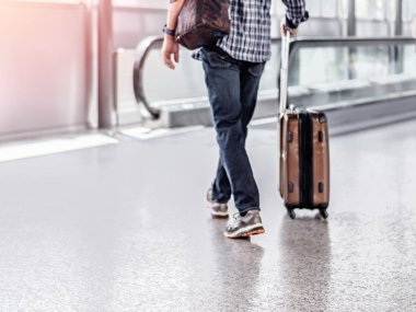 Havaalanı terminalinde elinde bavulla yürüyen tanınmayan bir adamın odaklanmamış fotoğrafı.