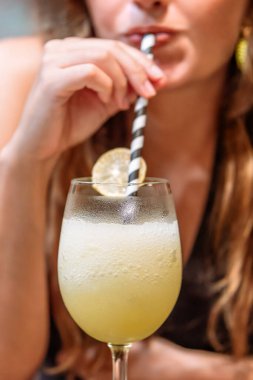 Bulanık bir kadın limon dilimiyle süslenmiş köpüklü limon kokteylini yudumluyor.