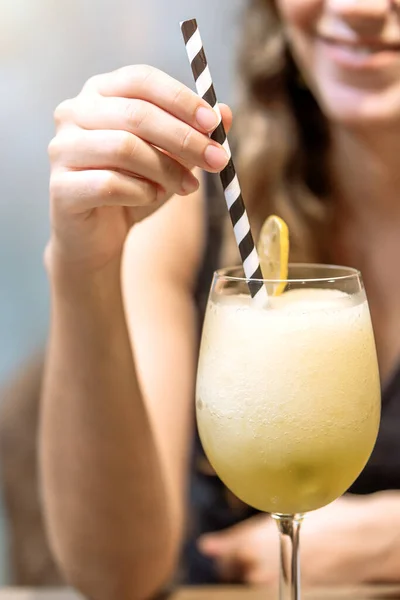 A blurred woman sips a frothy lemon cocktail adorned with a lime slice