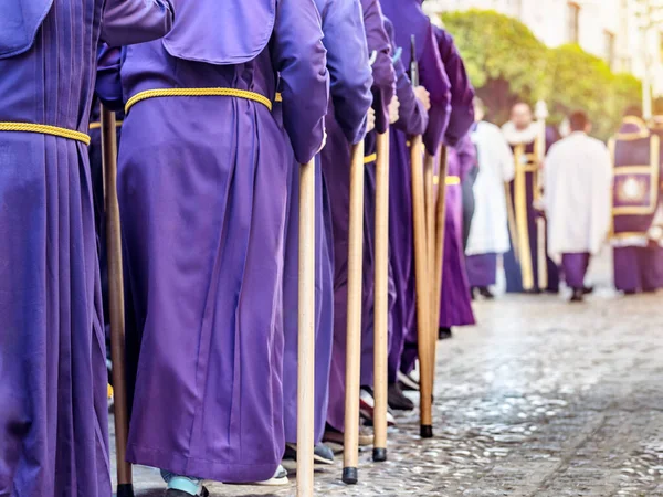 People in purple robes and yellow belts, holding wooden staffs during a procession. Selective Focus.