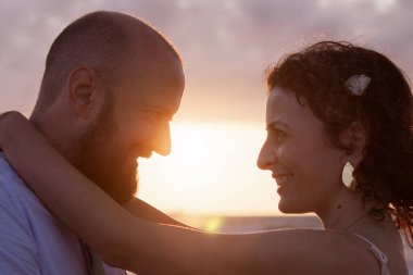 Bir çift kumsalda kucaklaşır, güneş arkalarında batar, ılık bir parıltı yayar..