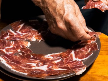 Uzman eller ustalıkla tabaktaki ince jamon dilimlerini düzenler..