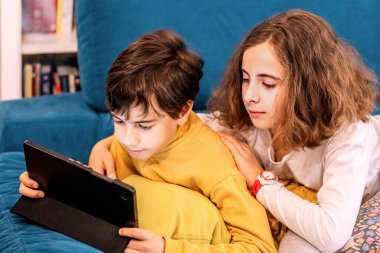 İki çocuk kanepede oturuyor, tabletle meşgul.
