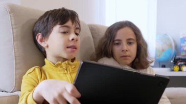 İki çocuk kanepede oturuyor, tabletle meşgul.