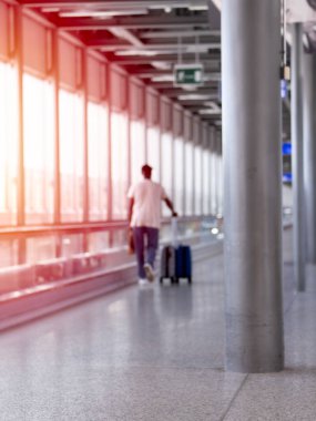 Havaalanı terminalinde elinde bavulla yürüyen tanınmayan bir adamın odaklanmamış fotoğrafı.