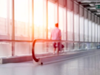 Havaalanı terminalinde elinde bavulla yürüyen tanınmayan bir adamın odaklanmamış fotoğrafı.