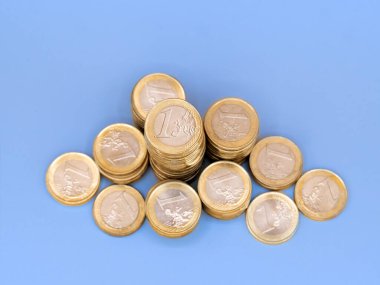 Mavi bir arkaplan karşısında 1 avroluk madeni para yığınları.