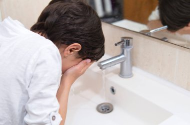 Lavaboda akan musluğun altında yüzünü yıkayan bir çocuk temizlik ve temizliğe vurgu yapıyor..