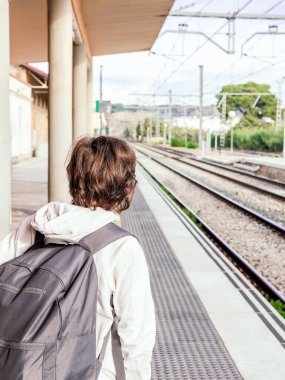 Sırt çantalı bir kişi tren istasyonunda bir platformda bekliyor..