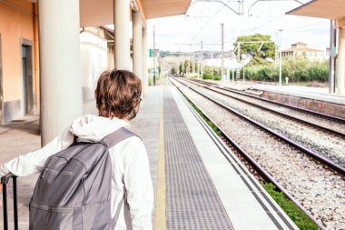 Sırt çantalı bir kişi tren istasyonunda bir platformda bekliyor..